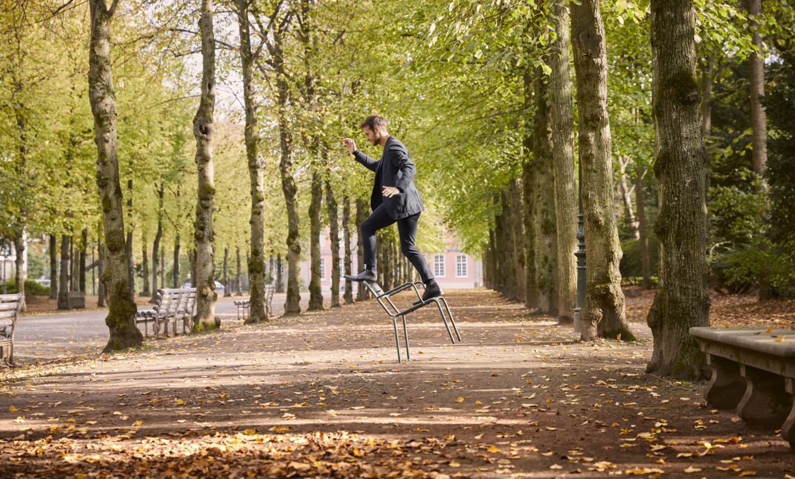 Mann balanciert auf einem Stuhl im Park in Düsseldorf