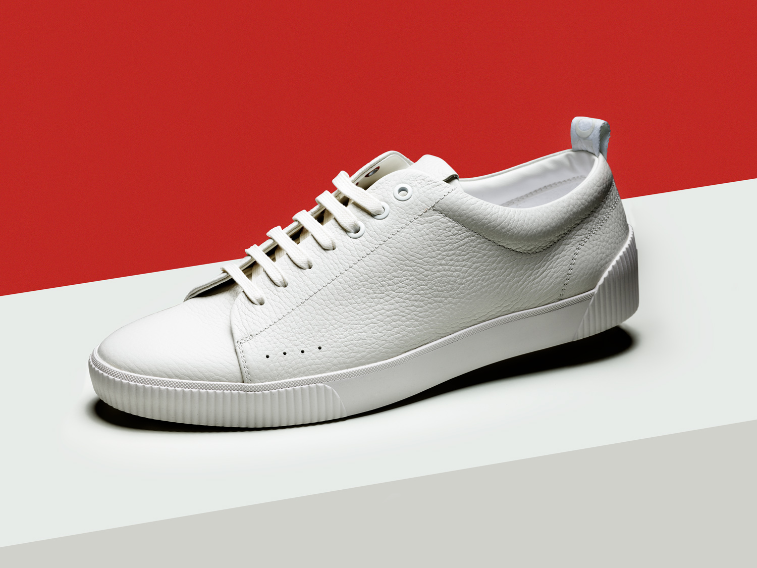 weißer Hugo Boss Schuhe vor roten Hintergrund. Produktfoto