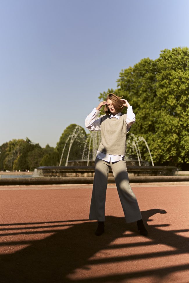 Eine junge frau steht steht im Sommer im Nordpark in Düsseldorf vor einem Wasserspiel und geht sich durch die Haare