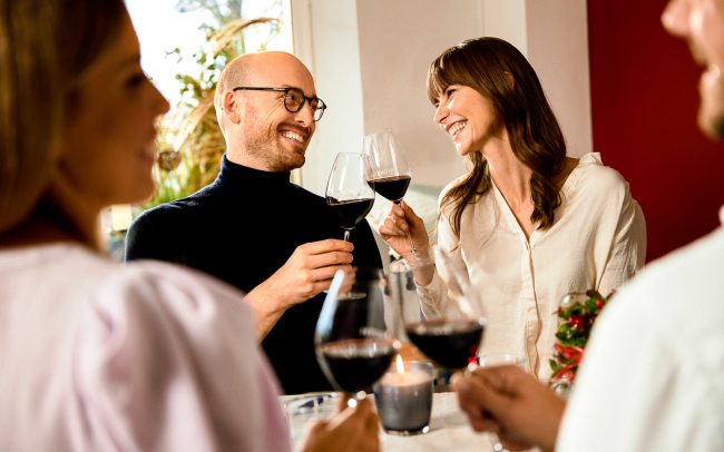 Eine Mann und eine Frau prosten sich mit einem Weinglas zu und lachen sich dabei an
