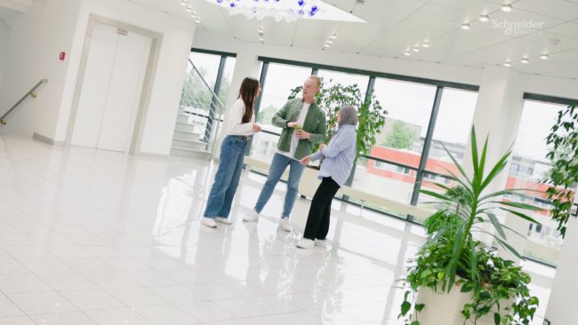 3 Junge Leute stehen in einem Bürogebäude zusammen